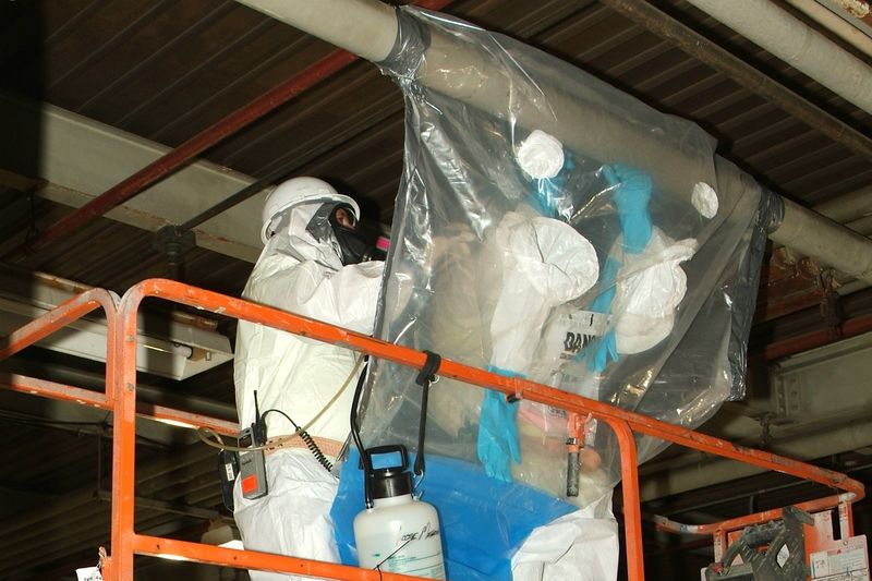 Trabalhadores com fato de proteção integral e máscara numa zona confinada de remoção de amianto